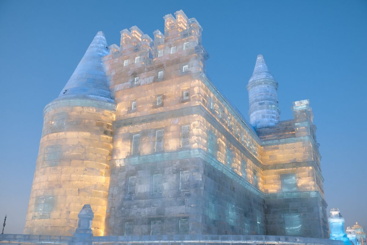 A large illuminated ice castle glowing against a clear blue evening sky.