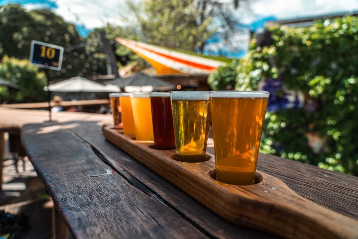 A beer flight displayed on a rustic wood table outdoors