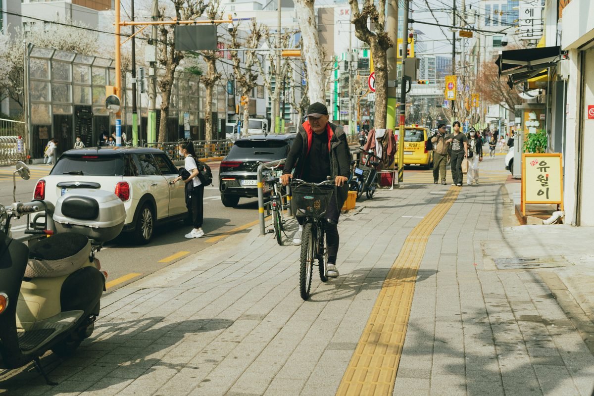 A man riding a bicycle along a busy city street sidewalk.