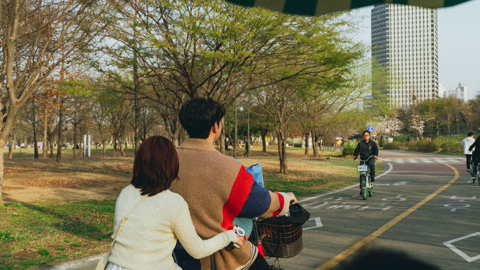 A couple cycling together on a park path surrounded by spring trees.