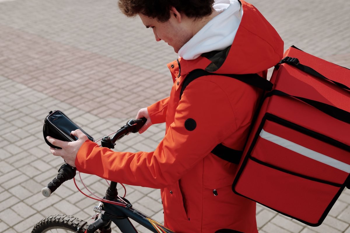 A food delivery worker checking a smartphone mounted on a bicycle.