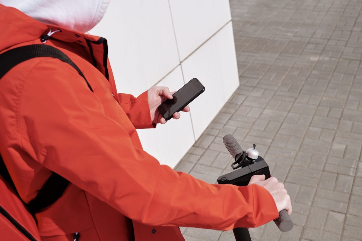 A person in an orange jacket interacting with a smartphone outdoors.