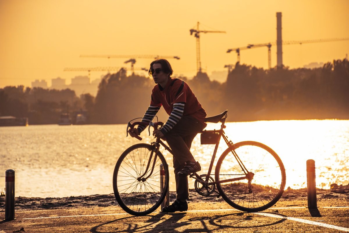 A person biking along a waterfront path during golden sunset hours.