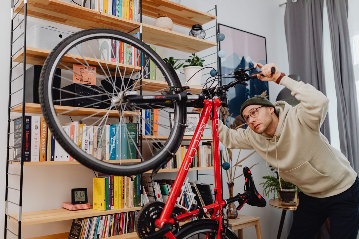 A person maintaining and inspecting a bicycle indoors near bookshelves.