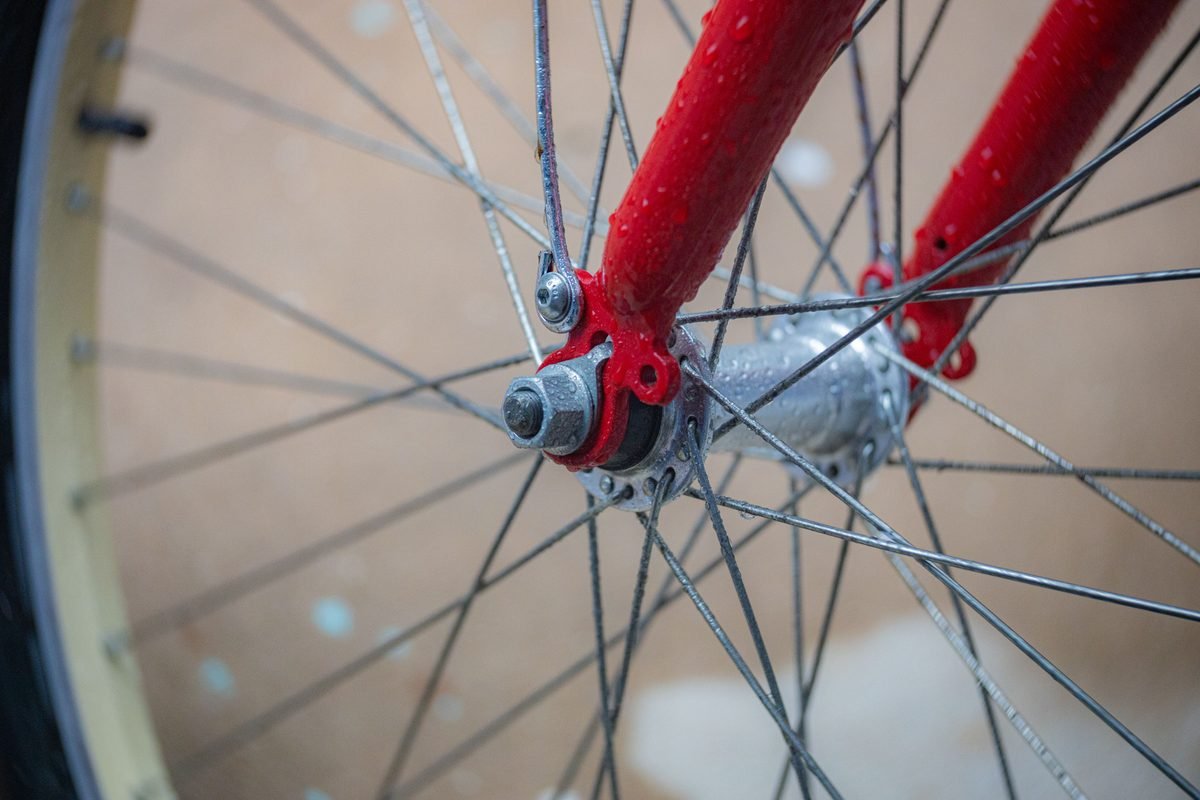 Close-up of a wet bicycle wheel with water droplets on the red frame.