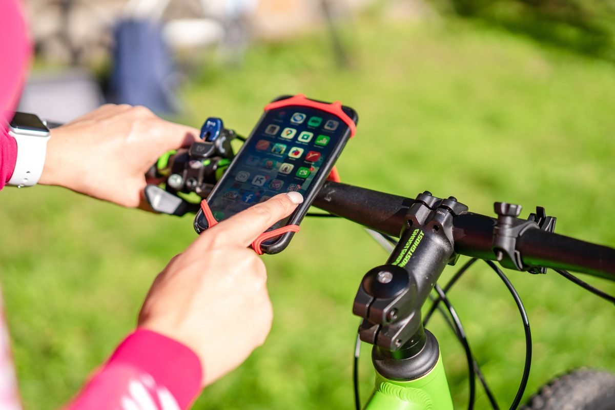 A cyclist using a smartphone mounted on bicycle handlebars outdoors.