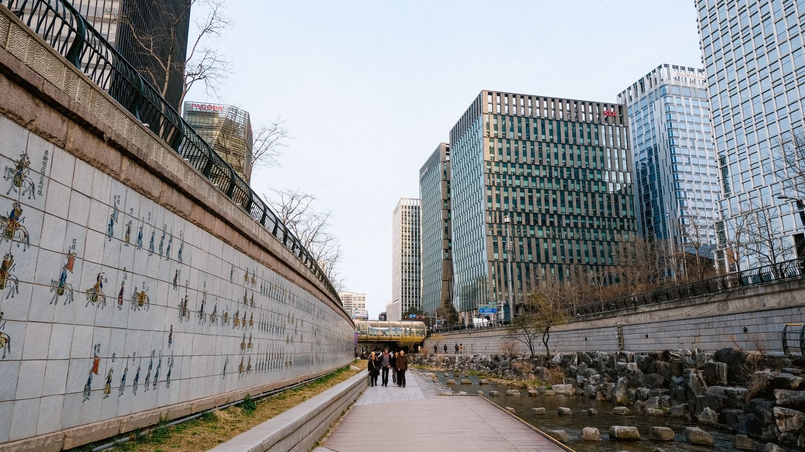 Modern skyscrapers overlook the pedestrian walkway along Cheonggyecheon Stream in Seoul.