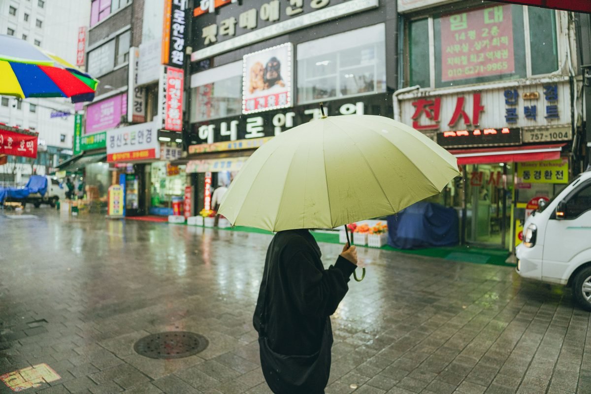 A person holding an umbrella walking down a rainy street in Seoul
