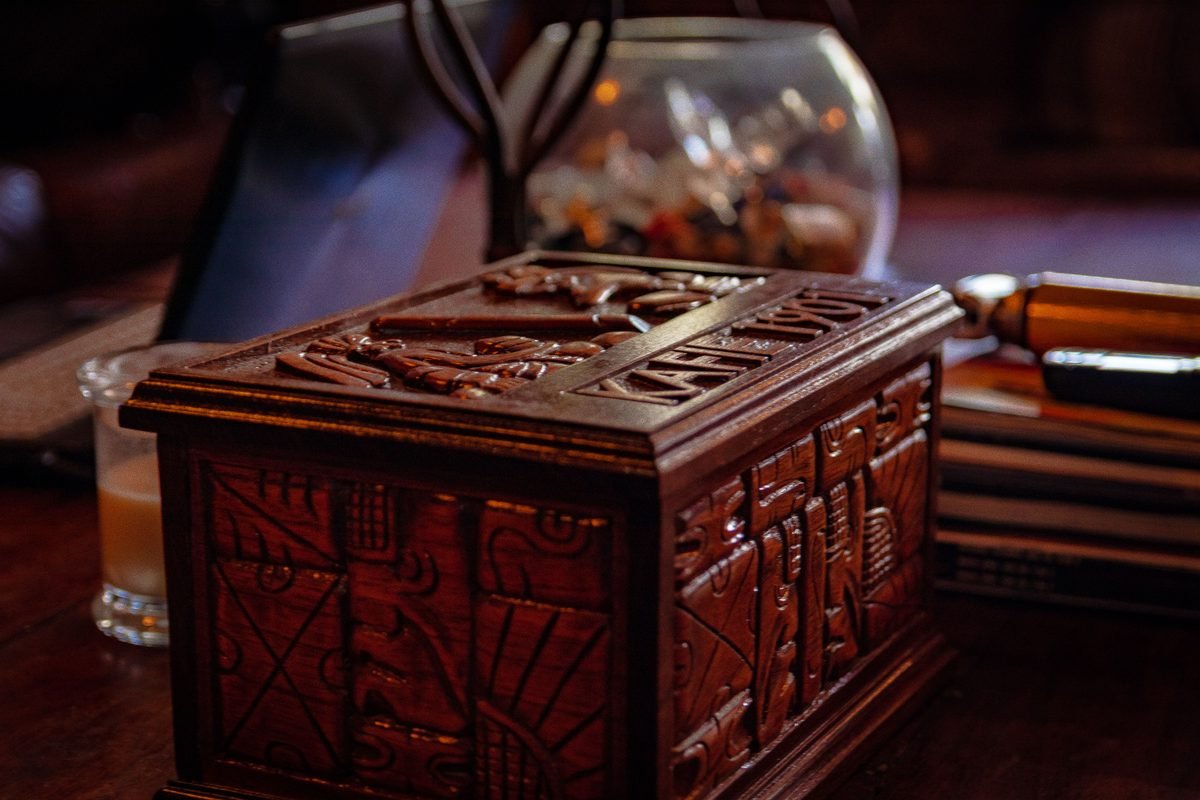 An intricately carved dark wood antique box resting indoors on a wooden surface.