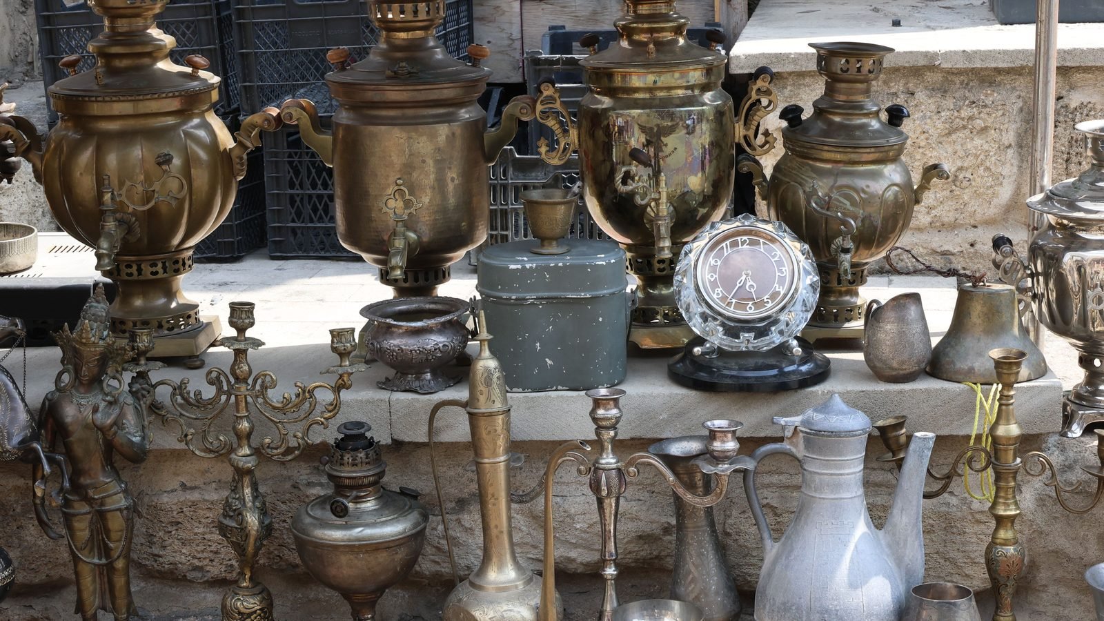 Collection of vintage brass samovars and metalware displayed on a stone surface outdoors.
