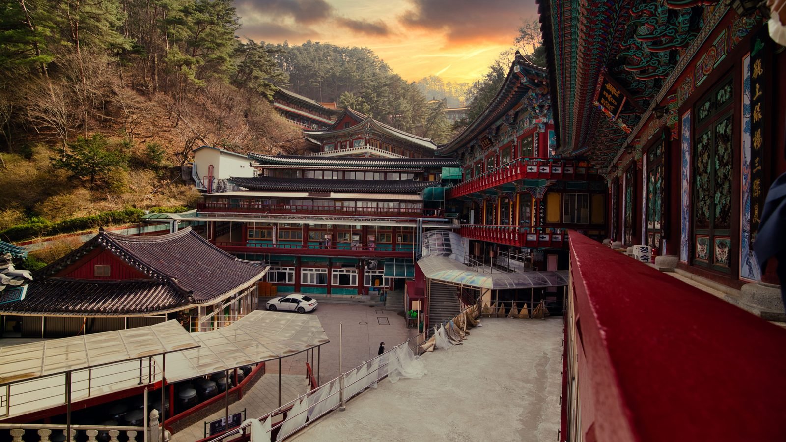 Traditional Korean Guinsa temple complex nestled against a lush mountain forest at sunset.