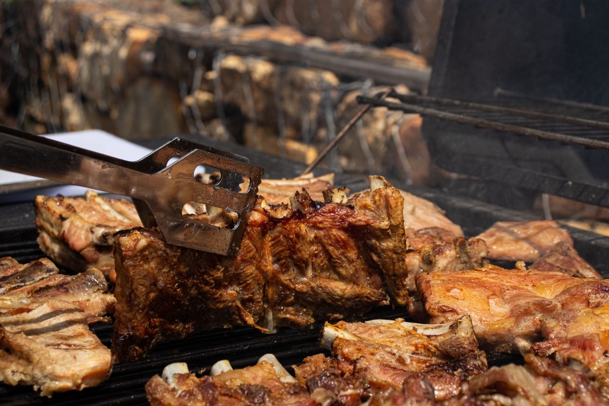 Pork ribs being grilled outdoors with tongs