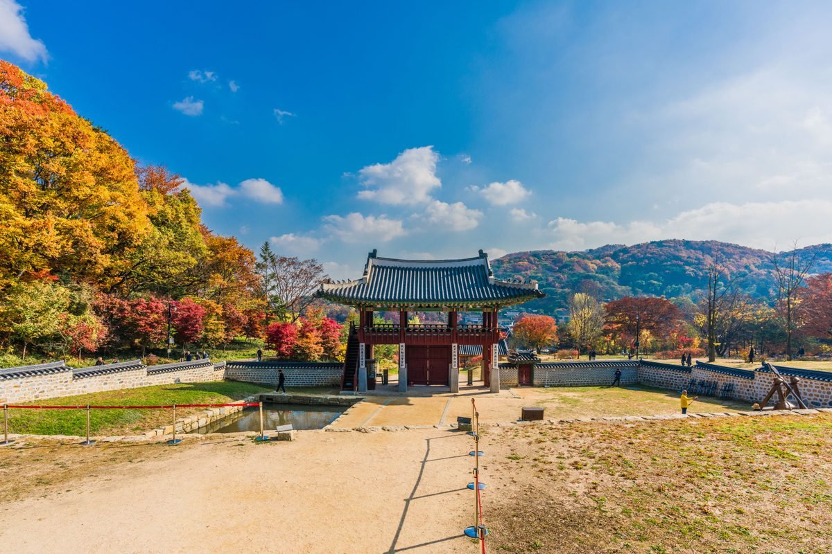 Traditional Korean gate framing autumn foliage and stone walls under blue sky