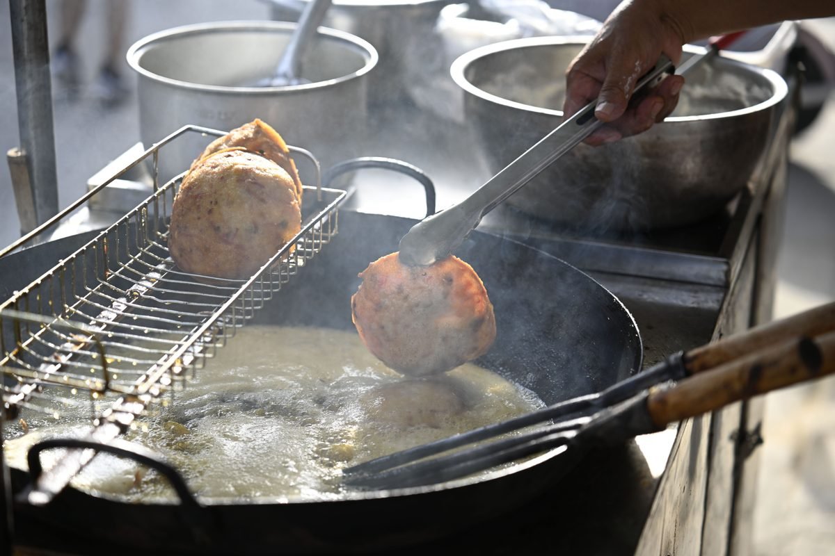 Street vendor frying food with tongs at an outdoor market.