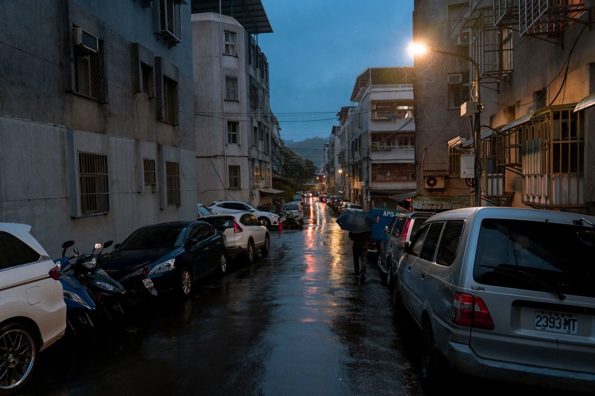 Wet urban street at night with parked cars and glowing lights.