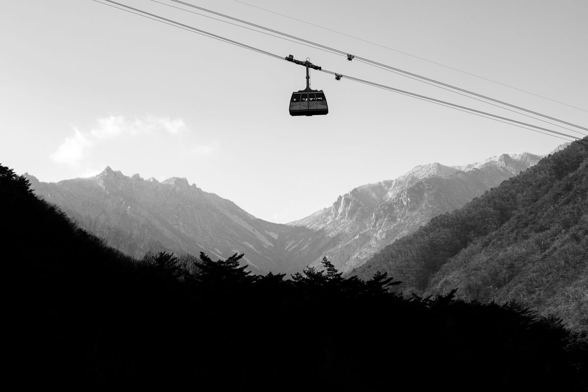 A cable car cabin moving against a mountainous backdrop in monochrome