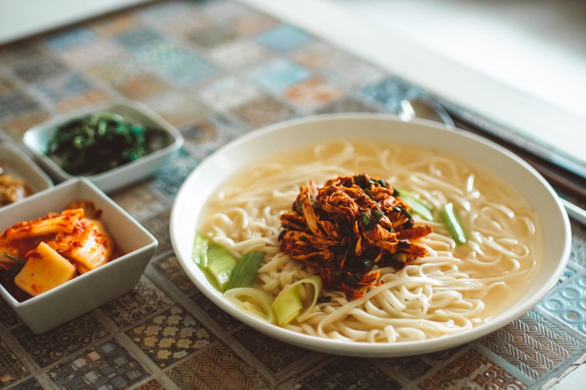 A bowl of Asian noodles served with side dishes of kimchi.