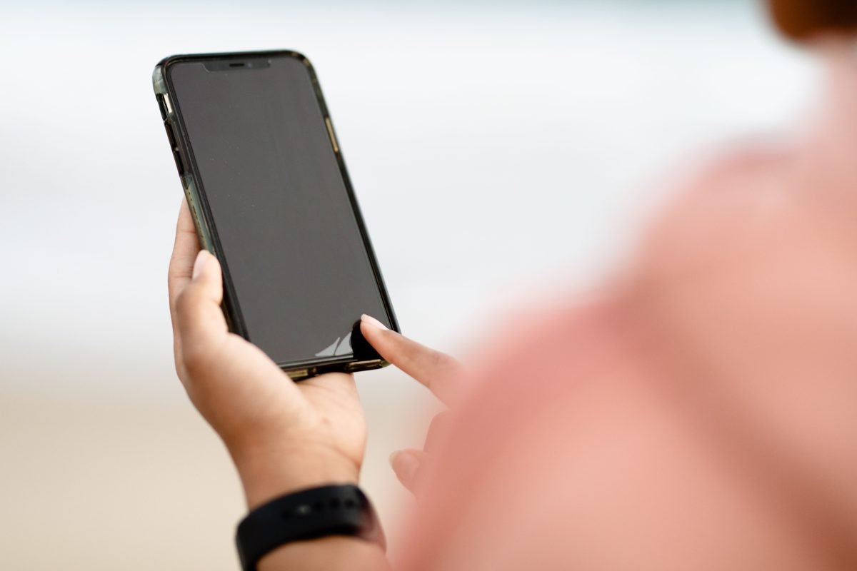 Hand interacting with a smartphone touchscreen outdoors.
